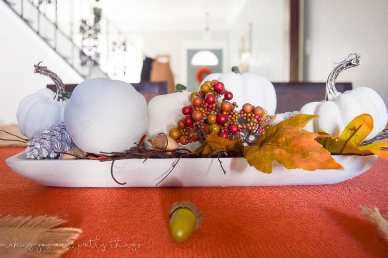 Another view of the dining room table fall centerpiece. A white dish holds faux white pumpkins, silver acorns, leaves, berries, and sticks.