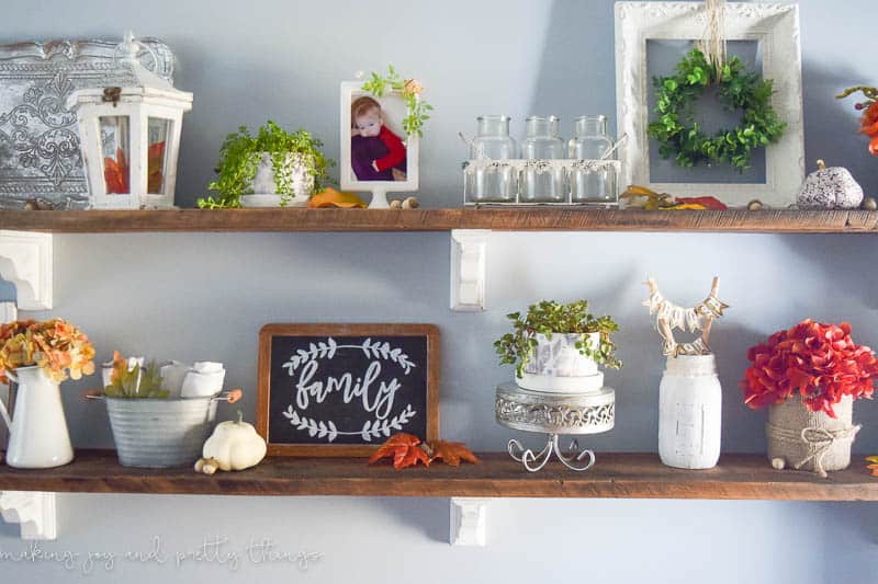 A look at all the traditional fall decor on our dining room shelves - picture frames, vases, faux flowers, greenery, and more sit on two dark wood shelves mounted to the wall.