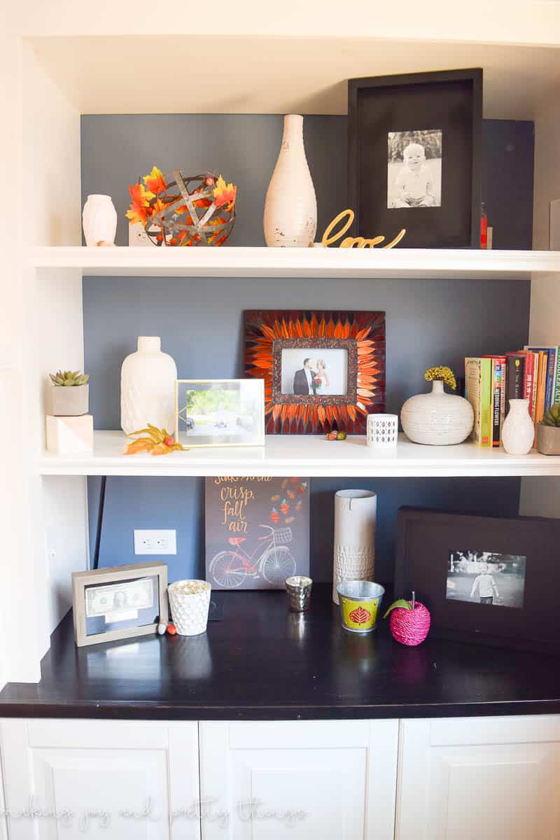 White built-in bookshelves decorated with picture frames, vases and other small every day decor items. Fall colors are sprinkled in with faux leaves, mini acorns and pumpkins.