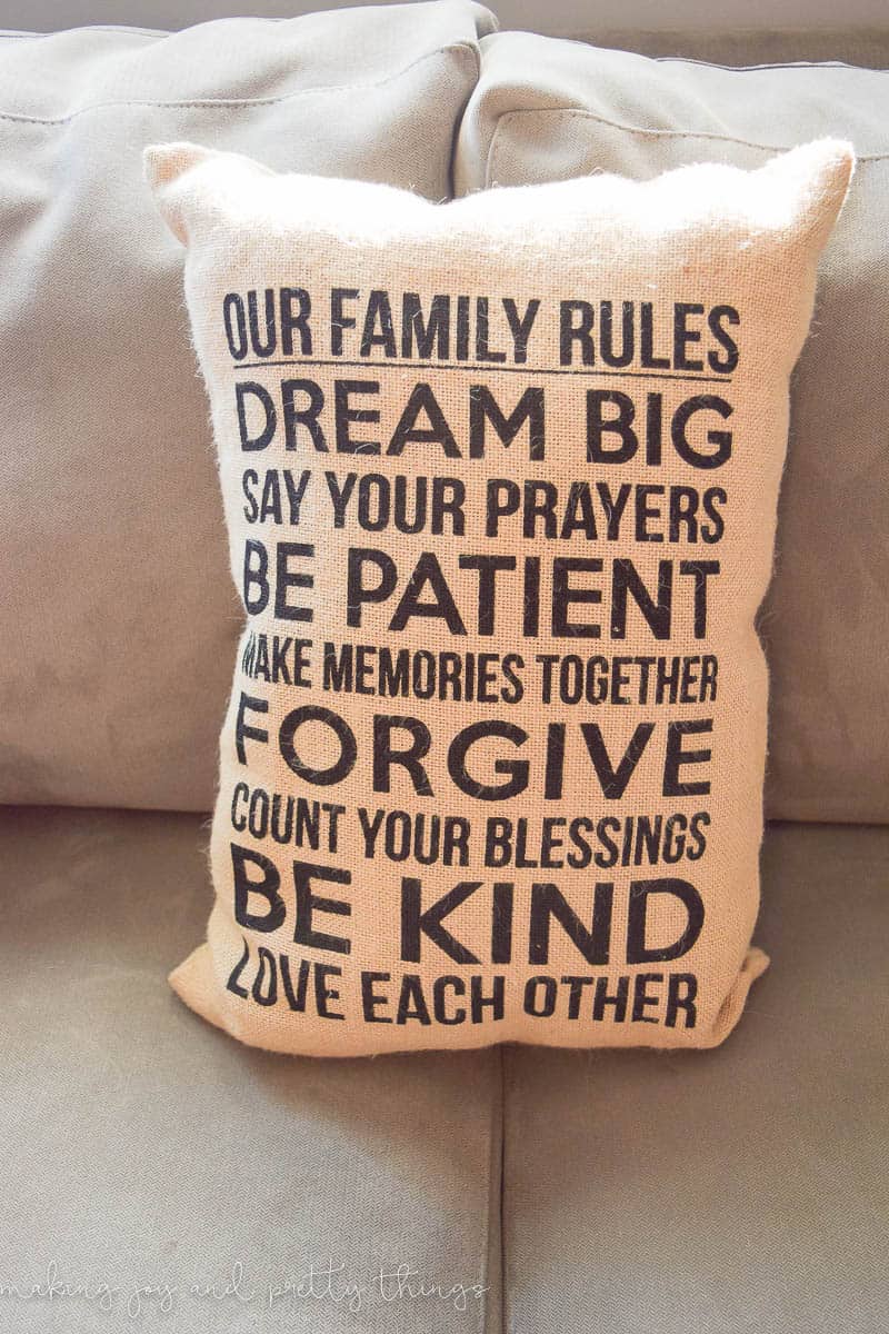 A burlap throw pillow with writing that says "our family rules: dream big, say your prayers, be patient, make memories together, forgive, count your blessings, be kind, love each other"