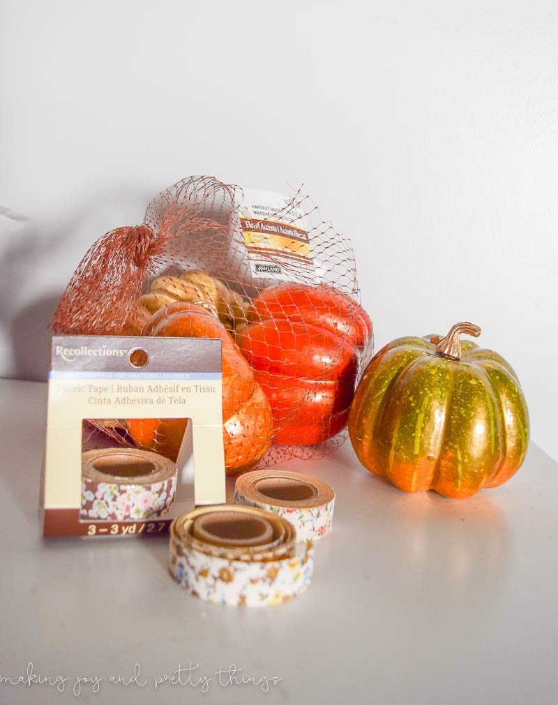 A bag of small faux pumpkins painted orange and gold, and a package of 3 rolls of floral washi tape sit on a white tabletop.
