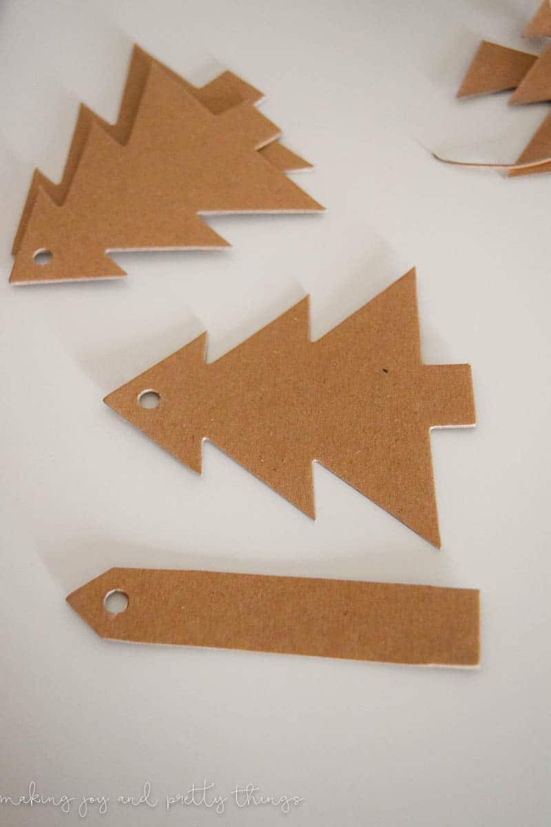 Small brown cardboard gift tags in the shape of a Christmas tree and a long rectangle, with small holes at the tips for string.
