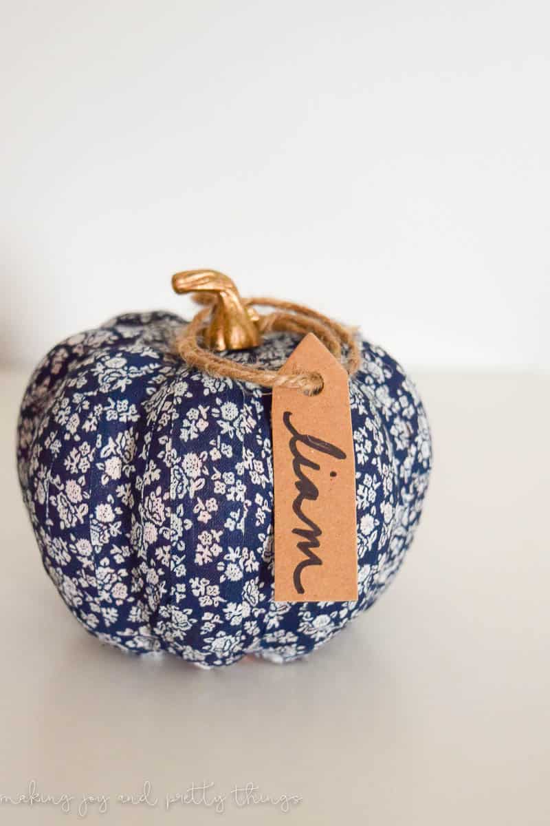 A washi tape pumpkin covered in a blue and white floral washi tape, with a cardboard name tag attached with brown twine string.