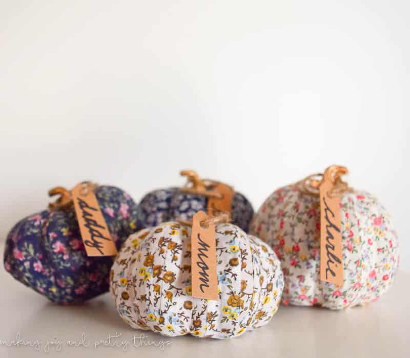 Five fabric washi tape pumpkins, each covered with different patterned floral washi tape, and each with a brown paper name tag attached to the stem with brown twine.