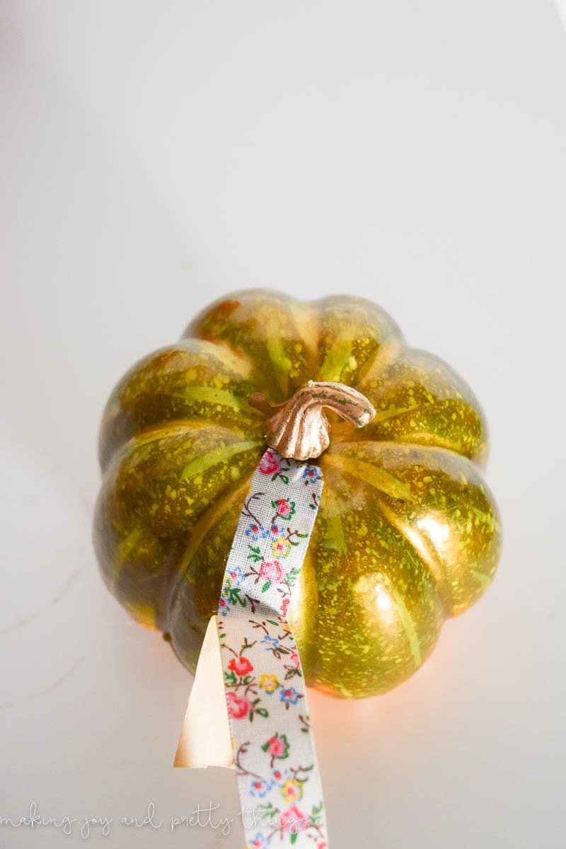 A small golf craft pumpkin with a strip of floral washi tape attached at the stem, going down the side of the pumpkin.