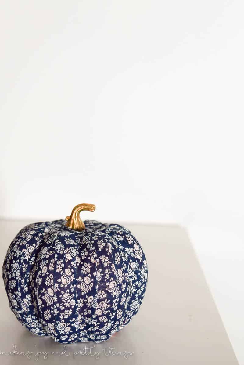 W small crafting pumpkin covered in blue and white floral washi tape, with a gold stem, sitting on a white tabletop.