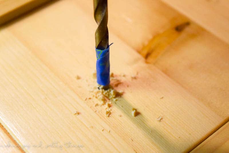 A close up image of a drill bit drilling a hole into unstained pine wood.