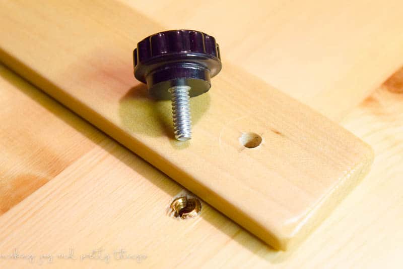 A small black knob with a threaded screw sits next to a pre-drilled hole on the craft able paper hold down arms.