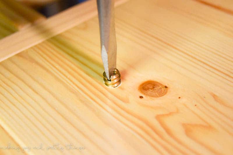 Using a flat-head screw driver to screw in a long threaded screw into the wooden tabletop.