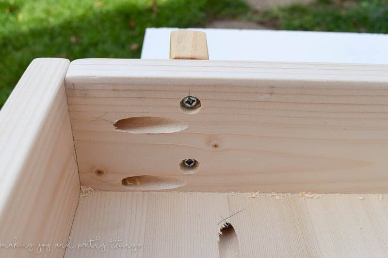 A close-up look at two screws drilled into the wooden underside of the crafting table. 