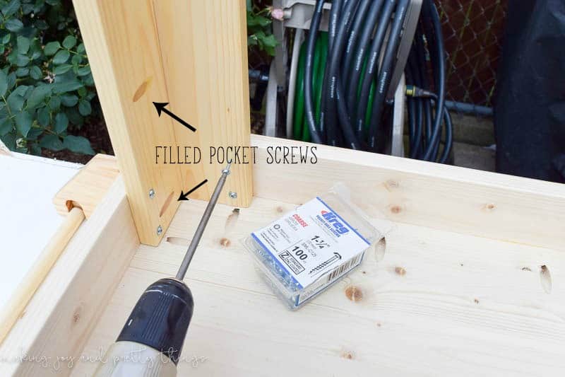 Attaching the table legs to the underside of the kids craft tabletop using a drill and pocket screws. Text imposed on the image says "filled pocket screws" pointing to two pre-drilled holes in the table legs.