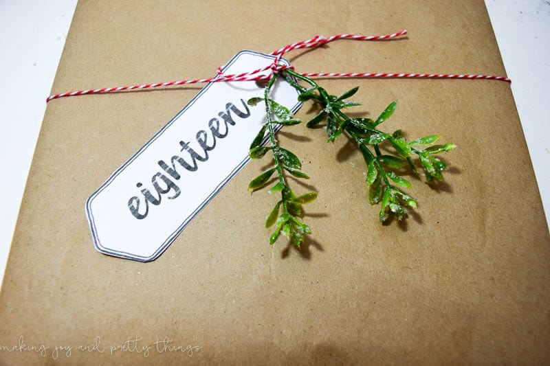 Christmas present wrapped in plain paper with a red and white twine and a christmas greenery used as a bow