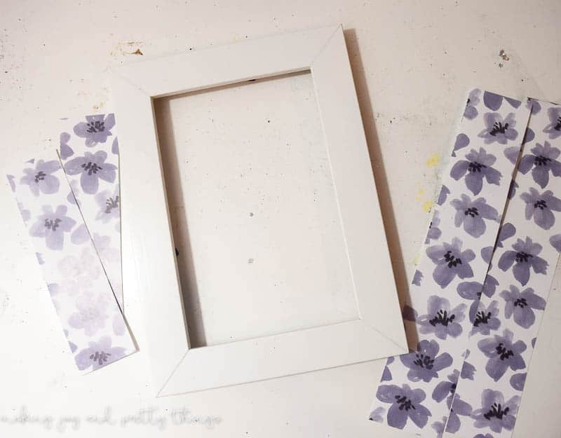 A single white picture frame surrounded by four strips of craft paper. The paper has a white background with gray and black illustrated flowers.