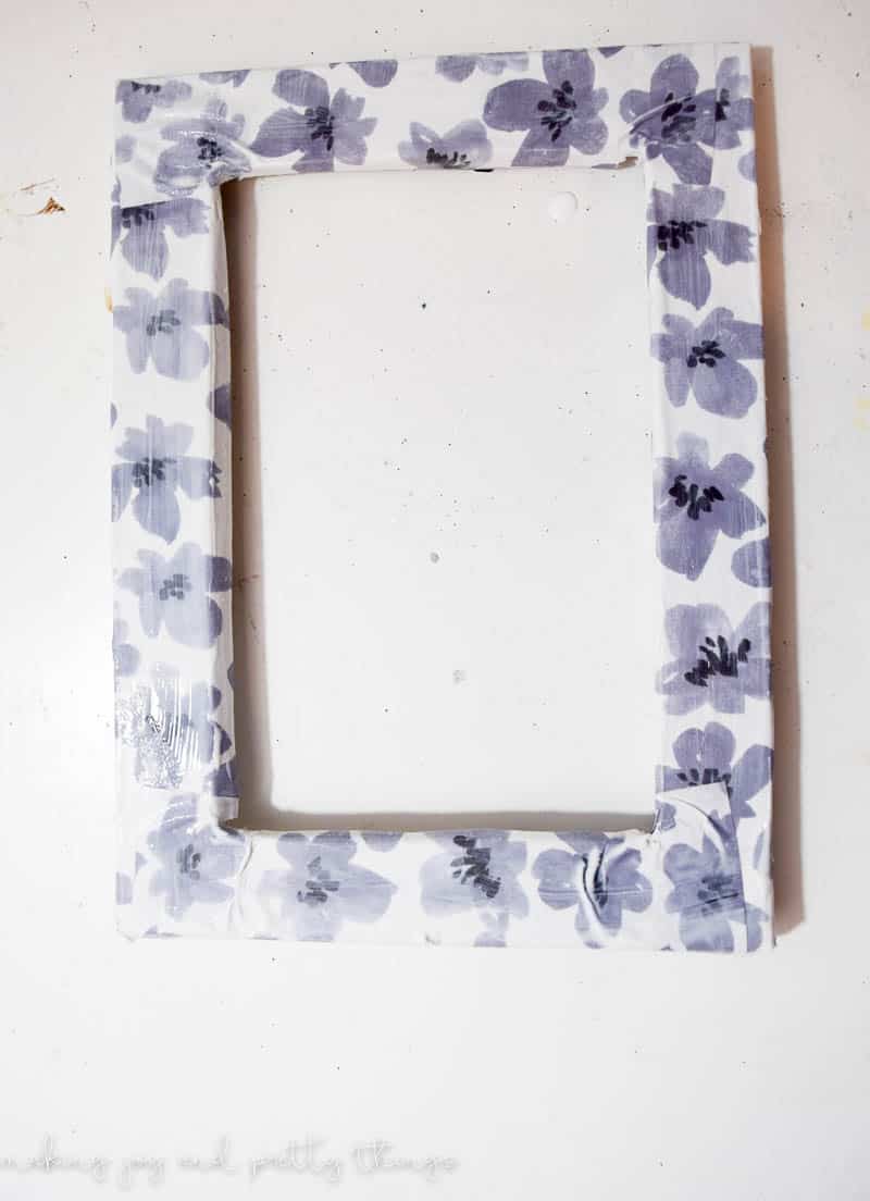 A picture frame covered in craft paper with a gray floral design. The craft paper has been attached to the picture frame with modpodge.
