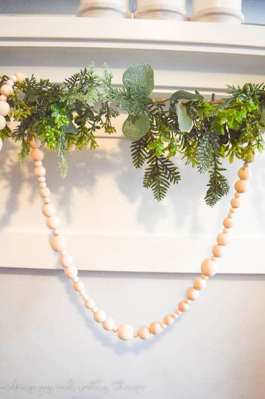 Decorating a mantle with garland to ad some Christmas flare to a living room using wooden beads
