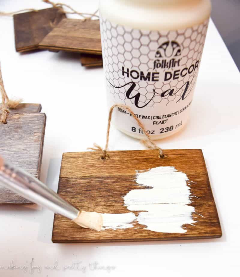 Using a small paint brush to apply the opaque white wax coating to the small pallet wood pieces. 