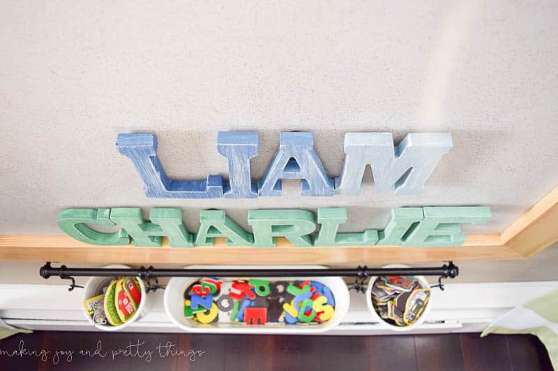 A photo of ombre distressed magnet letters for each little boy, with an IKEA kitchen storage system to hang fun buckets that are perfect for storing the rest of their magnets.
