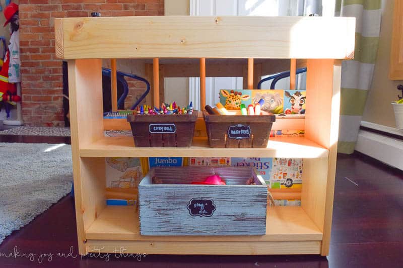 The shelves on the side of the crafting table provide storage for buckets of crayons, toys, and books.