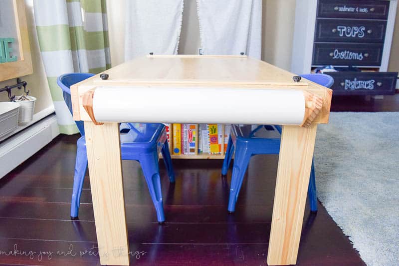 A wooden kids craft table complete with a paper holder to hold a reem of crafting paper for fun and convenient coloring.