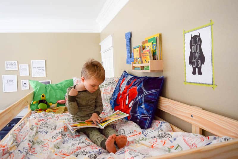 A boy's brother is reading in bed at the top of his bunk bed.