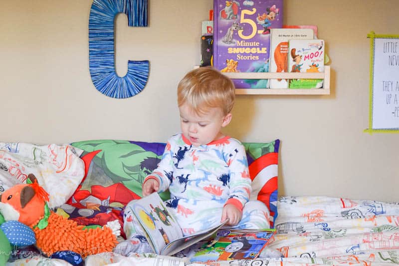 A boy is reading in bed with books piled up behind him.