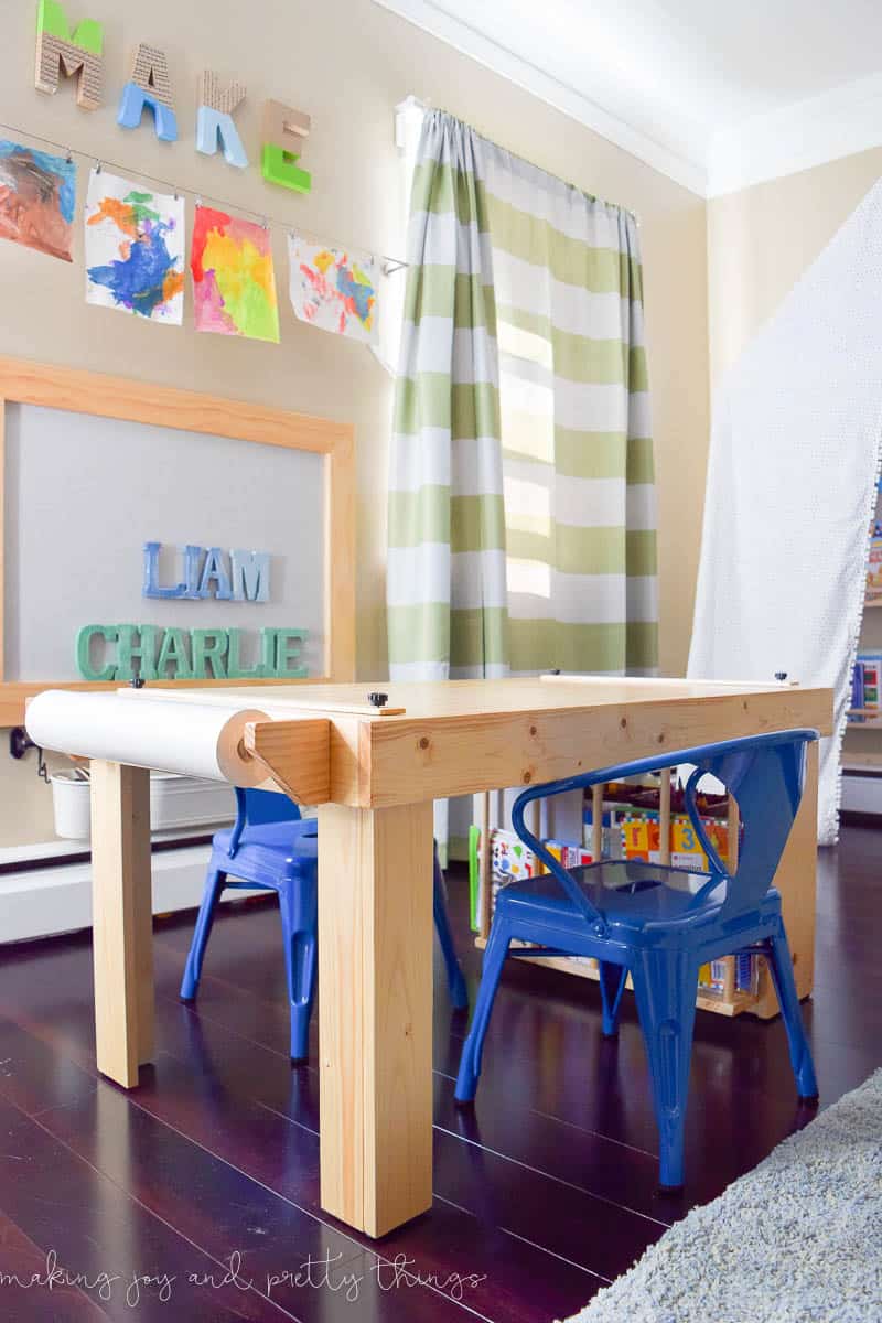 The finished crafting table, complete with a reem of paper attached to the paper holder, and two child-size blue metal chairs.