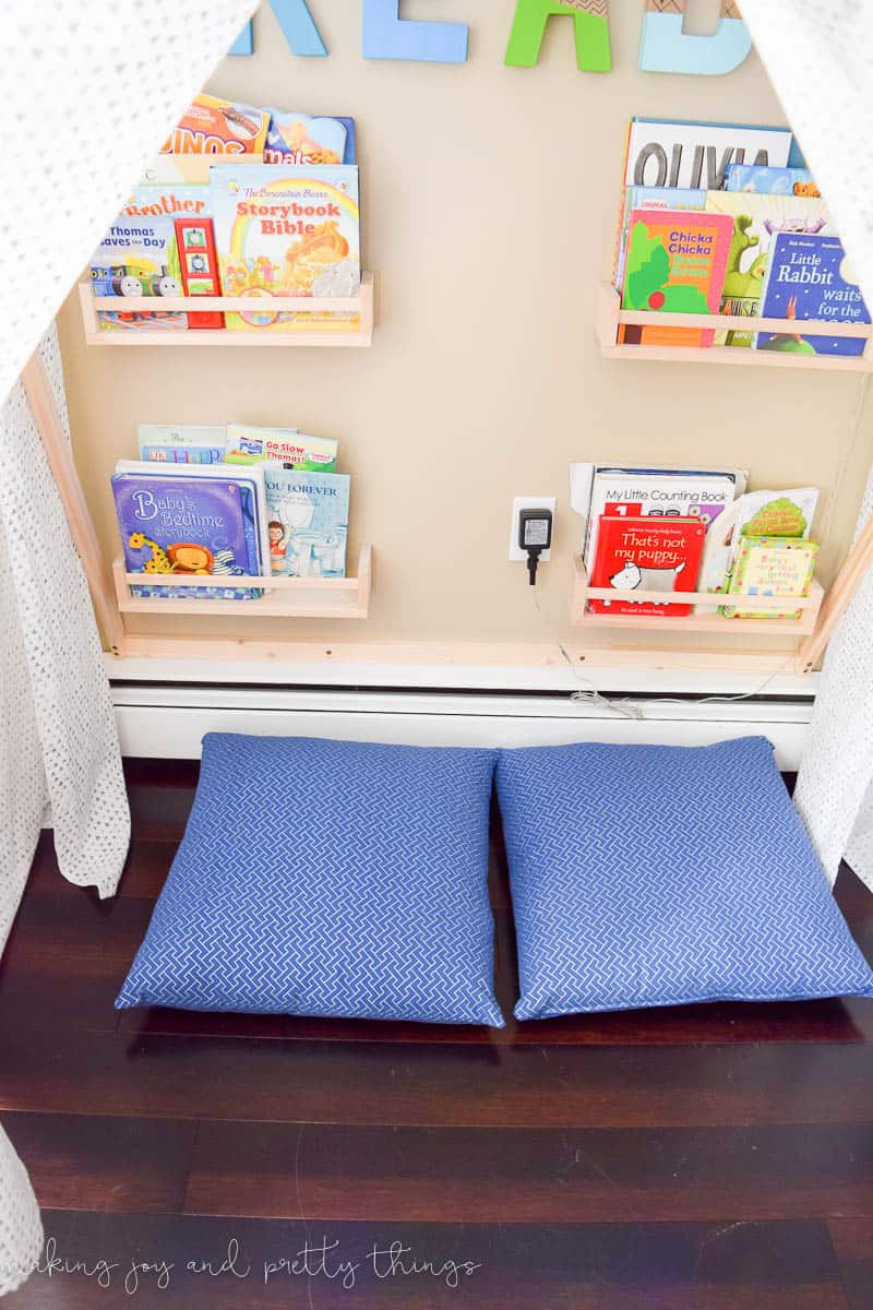 A photo of a DIY reading nook tent with bookshelves, showing the books and other items inside. The tent has 2 pillows on it.