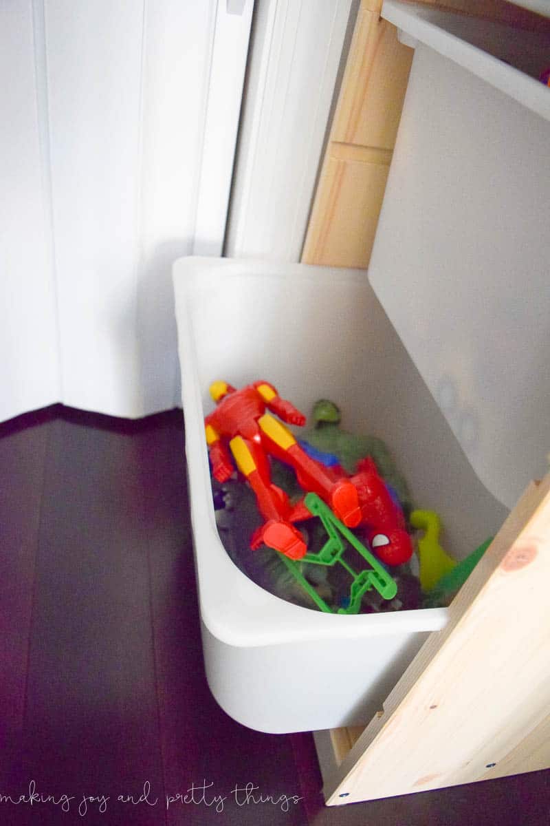 The photo of three bins of the storage unit are superheroes and other figurines, trucks/cars, and puzzles.