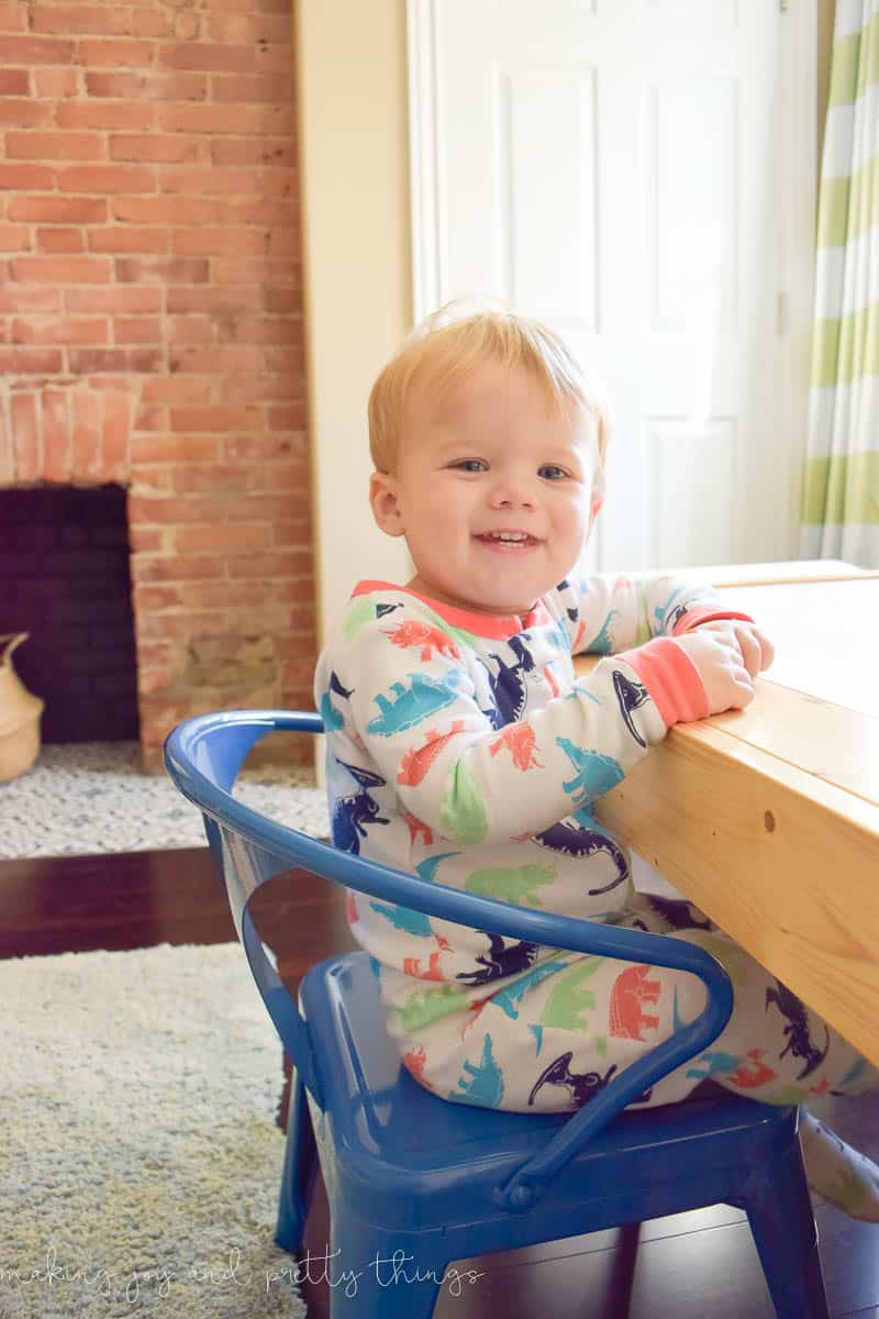 A smiling little toddler boy in dinosaur pajamas, happily playing at the DOY kids craft table in the playroom.