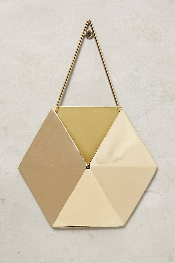 A gold hexagon shaped wall planter against a plain beige wall.