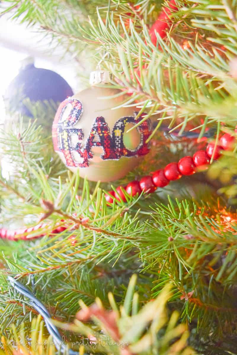 A close up look through the pine branches of a decorated Christmas tree, adorned with lights and garland. A round ornament with the word "PEACE" hangs on a branch.