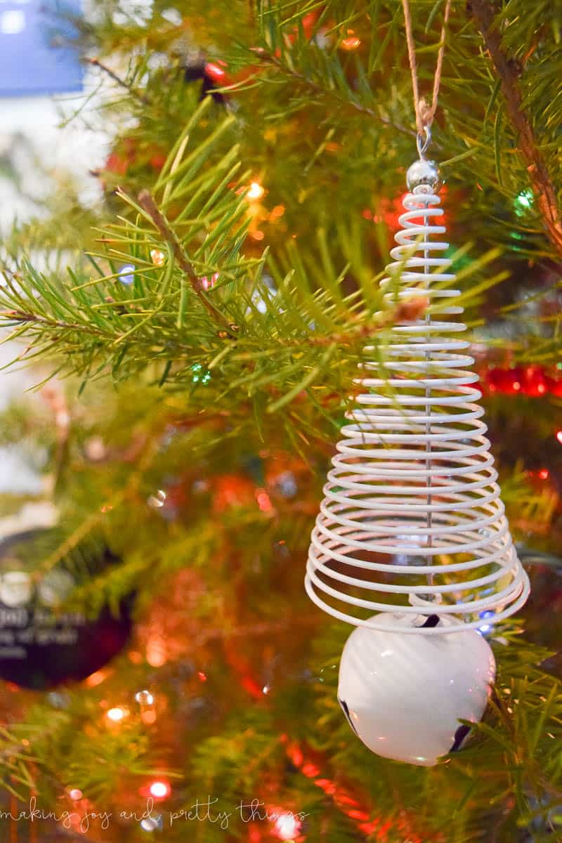 An abstract white wire ornament, wound into the shape of a tree, hangs on the pine branches of a Christmas tree, backlit with red lights.