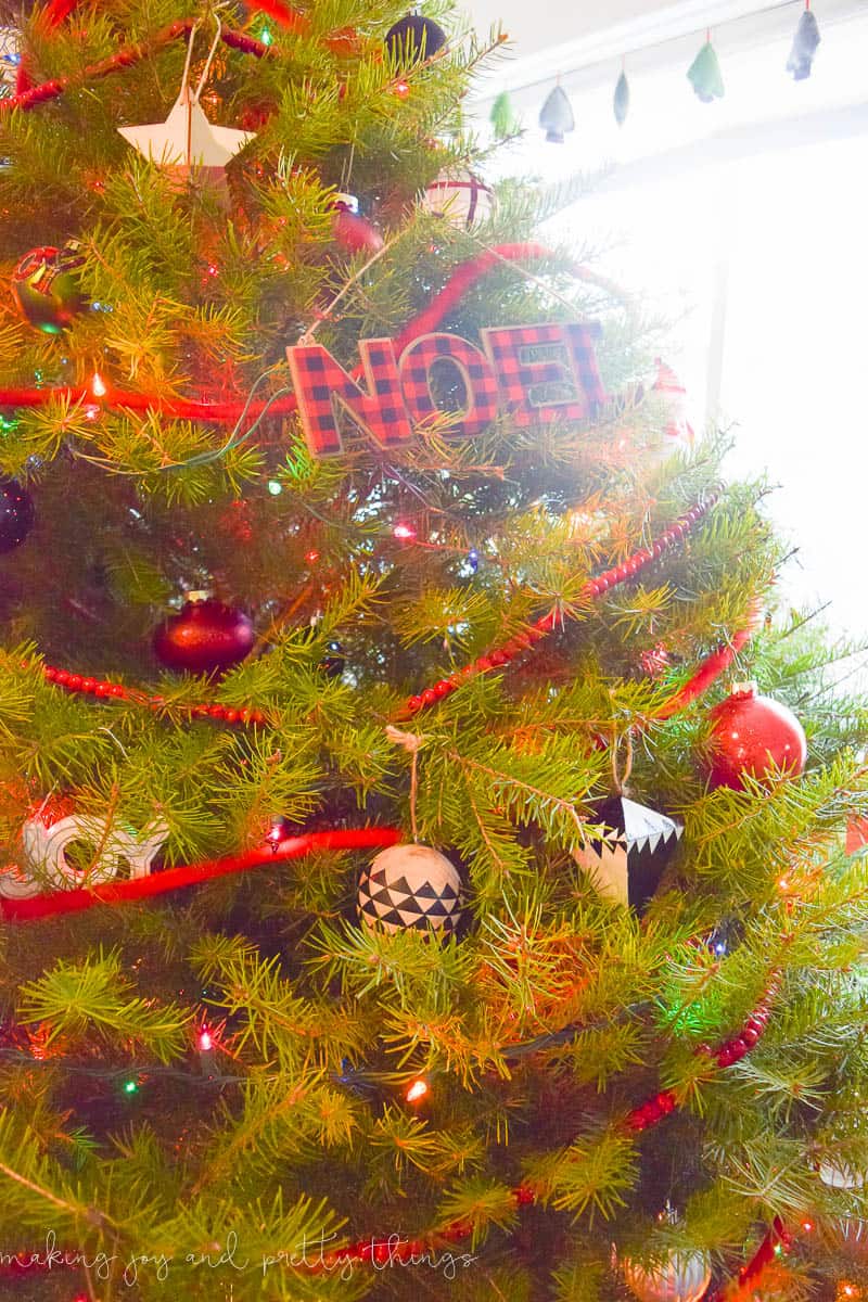 The branches of a fully decorated Christmas tree, adorned with a variety of red, white, and black Christmas ornaments, red and green Christmas lights, and red bead garland.