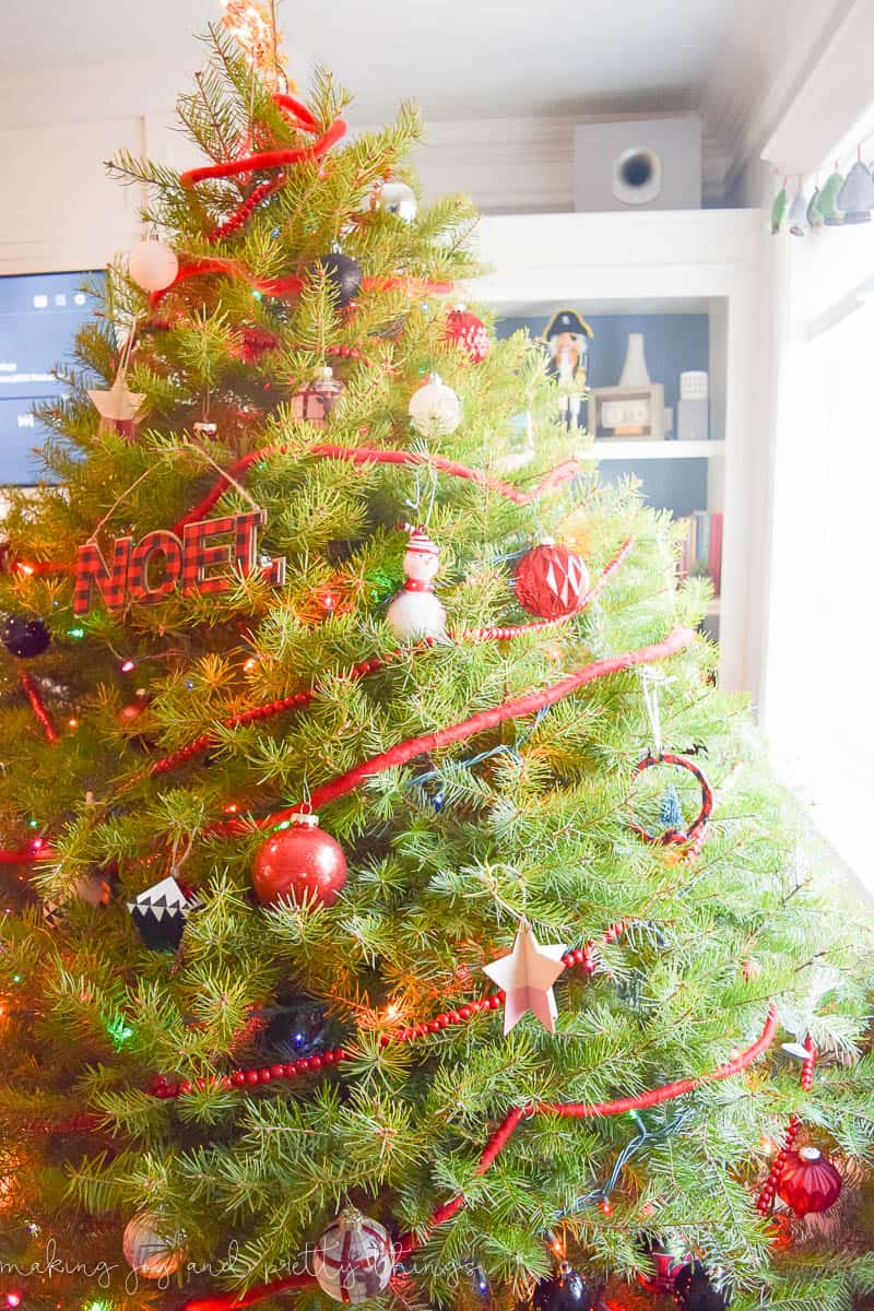 Another angle of the fully decorated Christmas tree, fully decorated with lights, garland, and ornaments. The sun from the window shines in on the tree, showing the fresh green color of the pine branches.