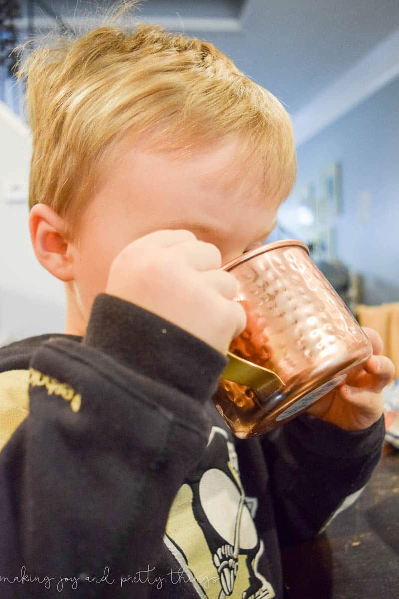 A young boy takes a big sip of hot chocolate from a brass mug.