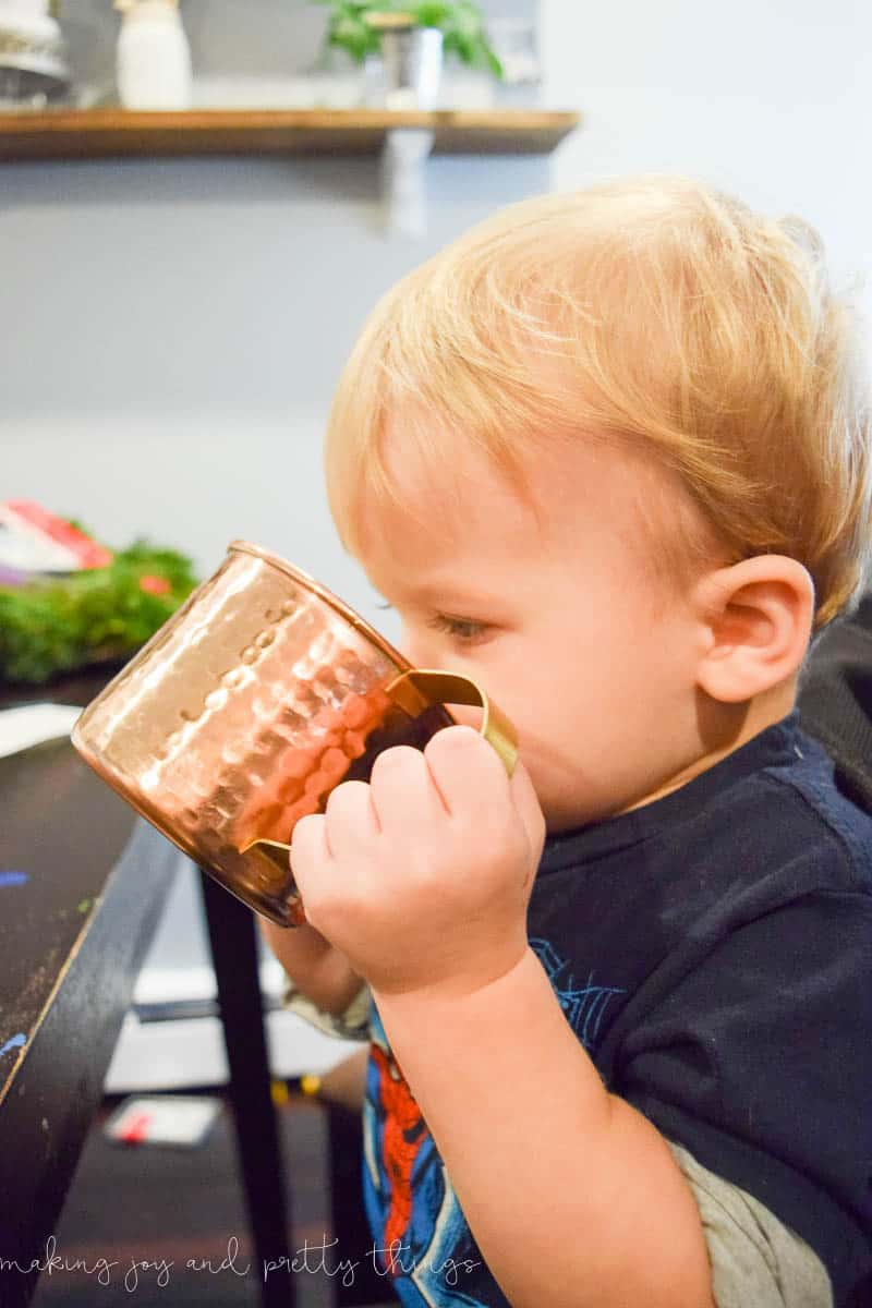 A young boy drinks a brass mug of hot chocolate during a break from decorating the Christmas tree.