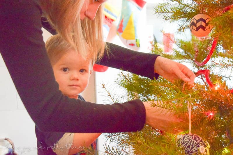 A young boy and and an older blond woman gently hang Christmas ornaments together on a Christmas tree.