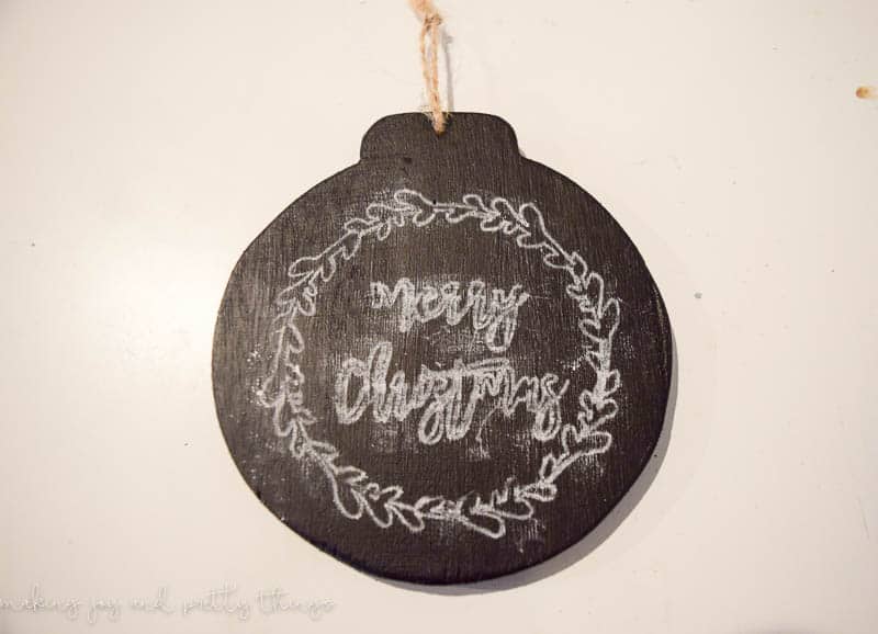 A black chalkboard ornament has a simple wreath design and the words "merry christmas" drawn on with white chalk.