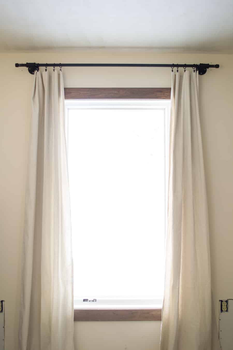 A complete look at the DIY pip curtain rod mounted to the wall, holding two white linen curtain panels.