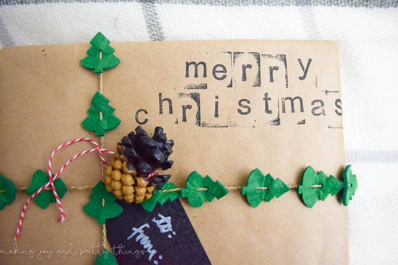A live the Christmas tree garland on this rustic gift wrapping! The finishing touch is the "merry christmas" stamping and paint-dipped pinecone gift tag.