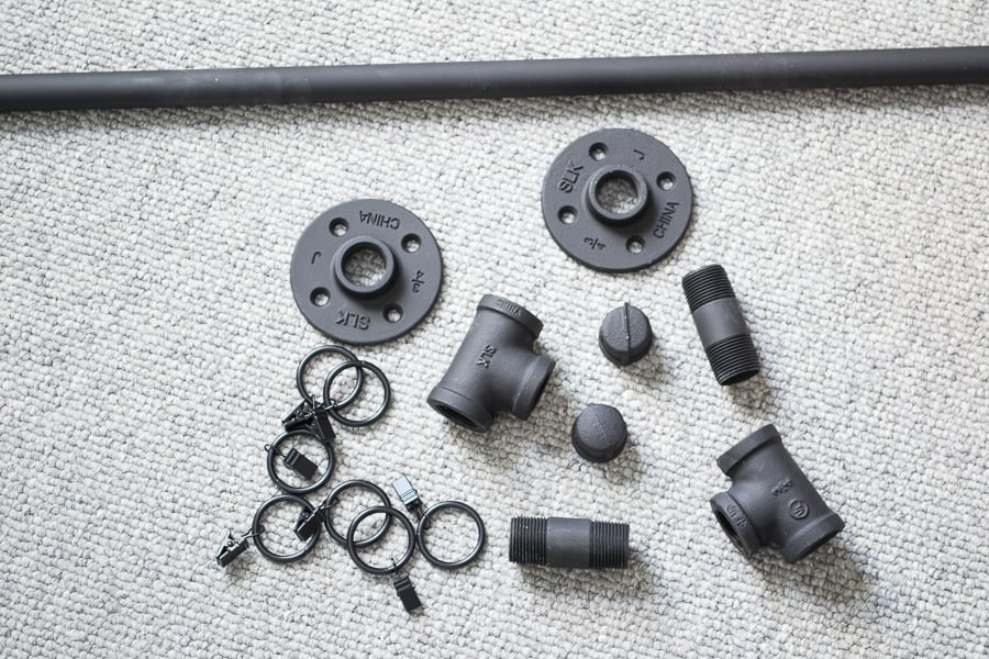 All of the matte-black metal pieces needed to make a DIY industrial style curtain rod.