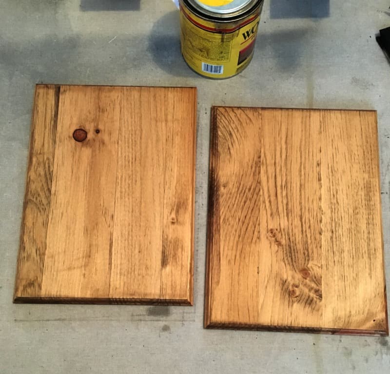 Two fully stained pine wood boards sit on a drop cloth work surface, drying.