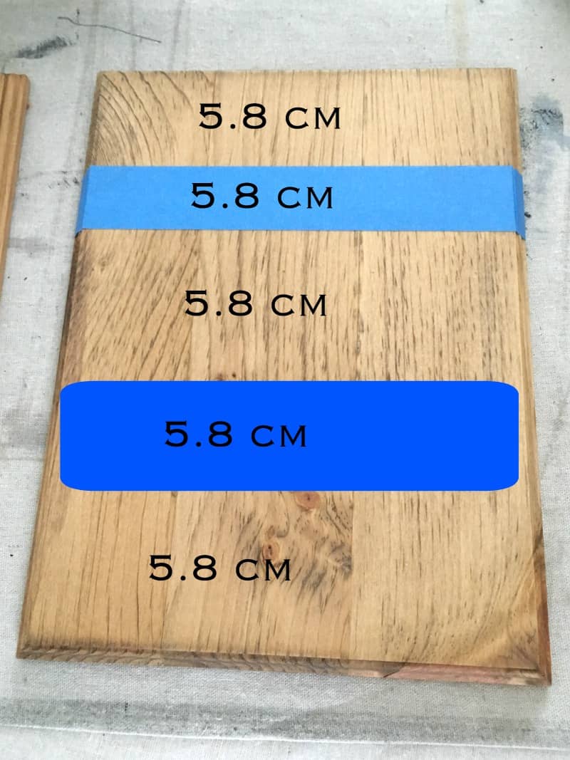 A pine wood board with stripes measured out in 5.8 centimeter increments. Two stripes of painter's tape and three stripes of natural wood are marked with "5.8 cm" text over the image.