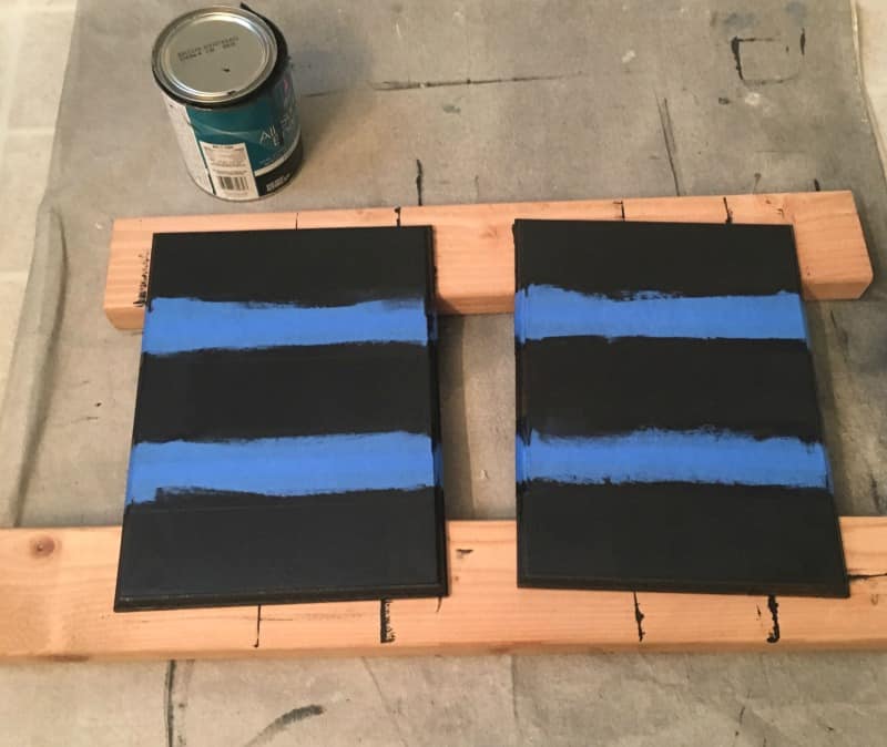 Two pine wood boards are painted mostly back, except for two stripes of blue painters tape on each board.