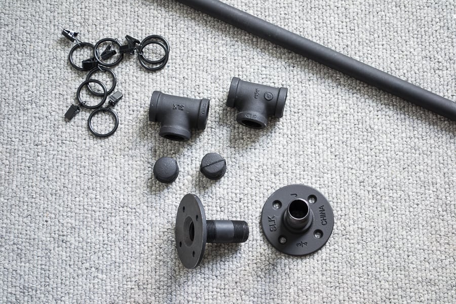 All of the pieces needed to assemble an industrial style pipe curtain rod, spray painted matte black, spread out on gray carpet.