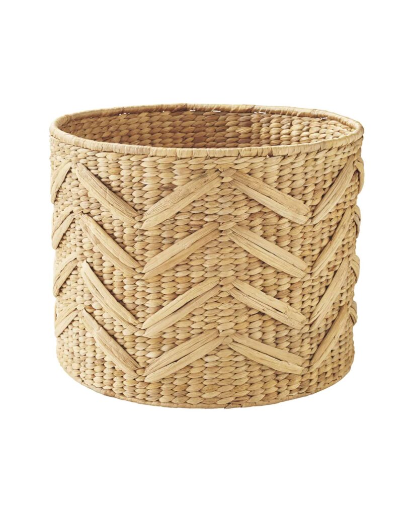 A tall, round woven storage basket in a natural wood color with a detailed zig-zag pattern.