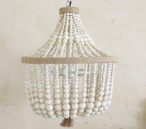 An off-white wood bead chandelier with two tiers, filled with strings of different size wood beads.