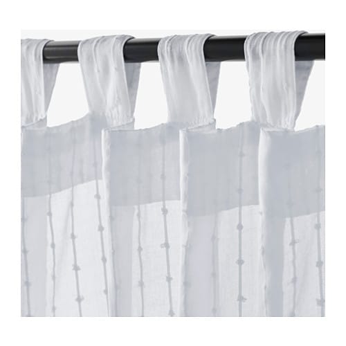 White linen curtains hang on a black curtain rod in front of a white background.