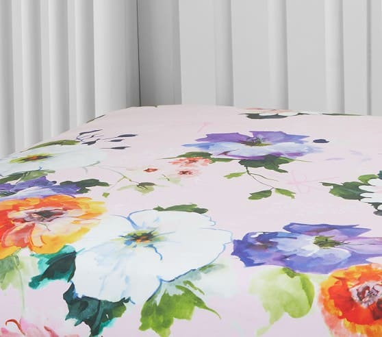 A crib mattress covered in a vibrant floral bedding with blue, orange, and purple watercolor flowers.