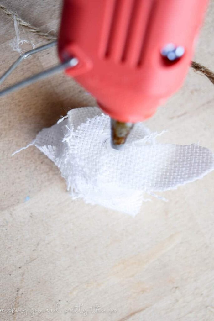 Attaching twin to make a garland to the back of a fabric flower with a hot glue gun and scrap piece of fabric to wrap around the twine